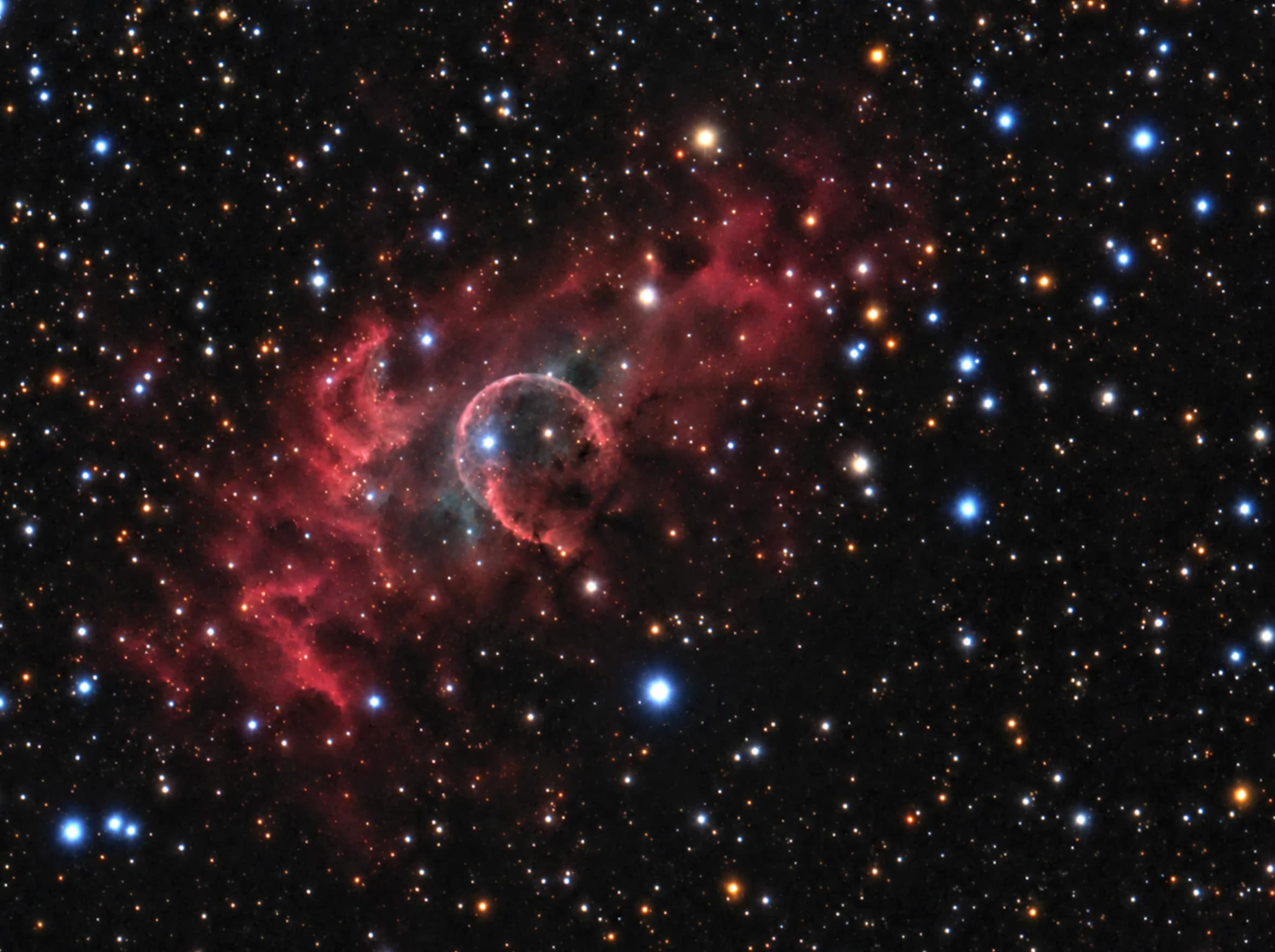A near-perfect sphere of gas glowing blue-white inside a much larger cloud of red hydrogen, surrounded by a dense field of blue and orange stars.